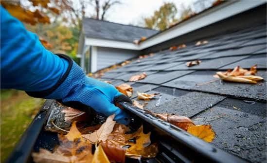 Gloved hand clearing leaves from a roof gutter